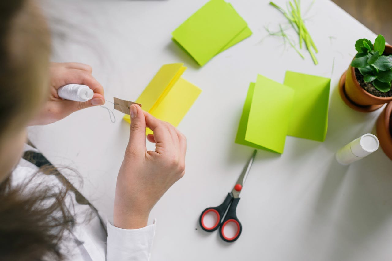 A person engaged in crafting, folding vibrant papers with tools on a desk.