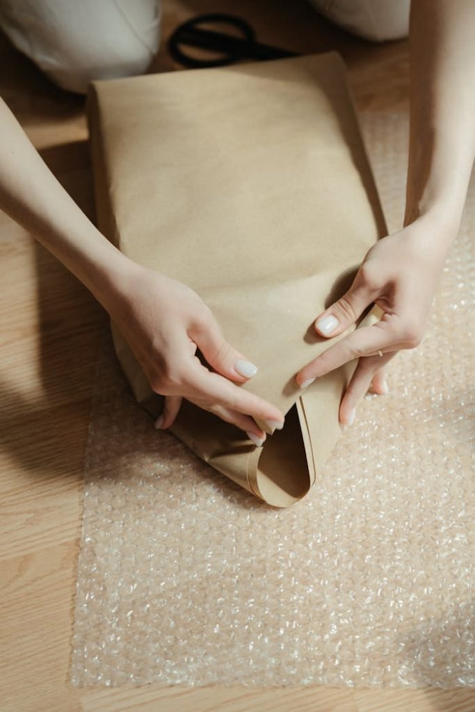 woman-in-brown-dress-holding-her-brown-leather-bag-4568735 Close-up of hands wrapping a package with protective bubble and kraft paper.